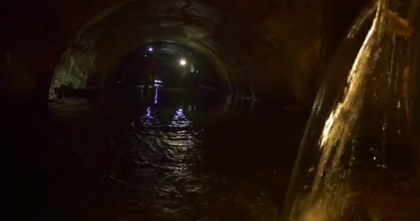 Мрачный тоннель с проливной водой и туристами, которые Уэйд вдоль него будучи на коленях глубоко в слизи и темной воде — стоковое видео