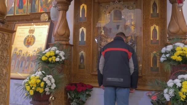 Vallásos ember megcsókolja egy ősi Saint Mary ikon, melyik borított-val pohár és két faragott fa oszlopok előtt — Stock videók