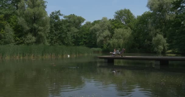 Deux hommes se reposent près d'un lac sur un pont en bois — Video