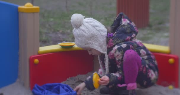 Mädchen in warmer Kleidung spielt im Sandkasten — Stockvideo