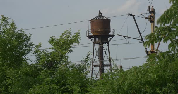 Una torre de agua de 1950 rodeada de árboles verdes y un poste eléctrico, siendo disparada en verano en la hora del anochecer — Vídeos de Stock