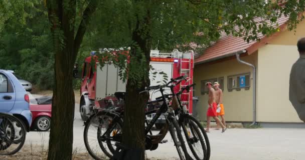 Um caminhão de bombeiros movendo-se ao longo do banco do lago Bolko em Oplole, Polônia. Turistas estão indo para trás e para a frente, e várias bicicletas estão esperando por seus proprietários . — Vídeo de Stock