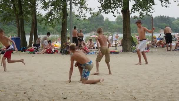 Los adolescentes están jugando al fútbol de playa en Bolko Lake con mucha gente descansando y aguas azules en el fondo, recibiendo disparos en Slo-Mo — Vídeos de Stock