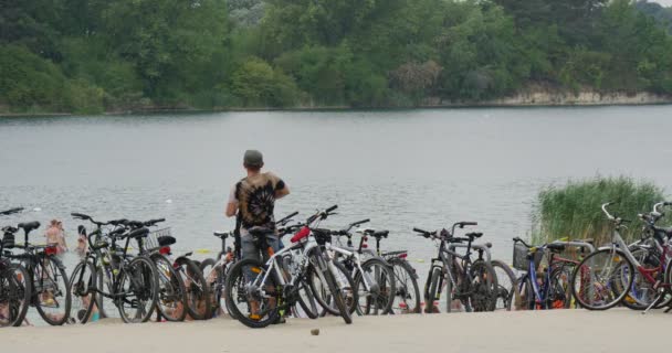 Un pintoresco lago Bolko con un montón de bicicletas, y un joven deportista protegiéndolos, mirando un impresionante agua de un pequeño complejo acuático — Vídeo de stock