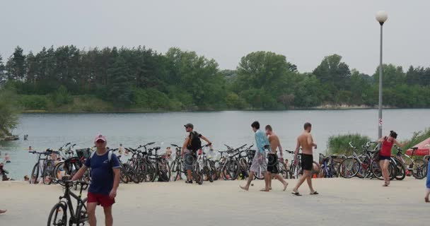 Un lago Resort con un montón de bicicletas en su orilla, con un montón de gente caminando allí, Estar en trajes de baño, y mirando un lago pintoresco — Vídeo de stock