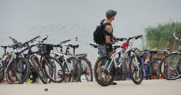 Ein lustiger Haufen Fahrräder am Ufer eines schönen Sees, mit vielen Menschen in Badeanzügen, die im Sommer hin und her fahren — Stockvideo