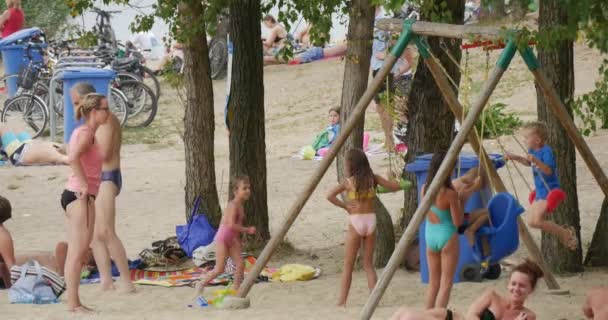 Niños balanceándose en un patio de recreo del lago Bolko con sus padres de pie cerca, vistiendo trajes de baño — Vídeos de Stock