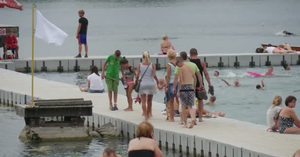 Un muelle de hormigón blanco Pisturesque del lago Bolko con un montón de turistas, mirando las aguas azules y la bandera blanca en el día en verano — Vídeos de Stock