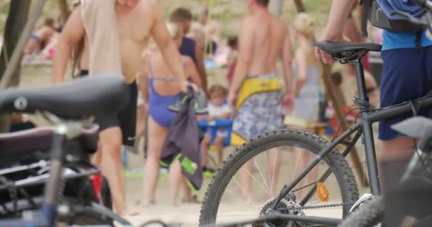 Dos bicicletas en el frente y varios niños balanceándose en un patio de recreo con sus padres, de pie en el fondo en verano — Vídeo de stock