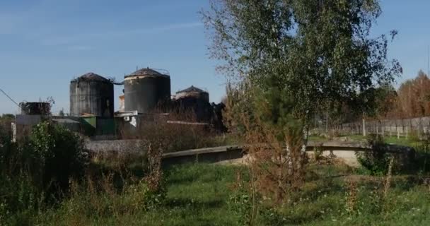 Um reservatório de armazenamento de óleo parecendo enferrujado, torre de guarda sombria e uma cerca com arame farpado e pólos de concreto protegendo-o na Europa Oriental no verão . — Vídeo de Stock