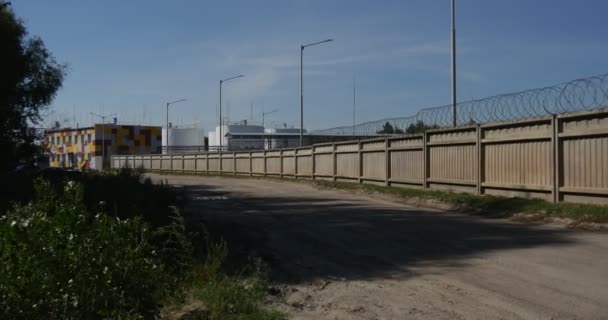 Langer Betonzaun mit Draht darauf, der die Öllager schützt und im Sommer abends mit einer Steadicam-Kamera aufgenommen wird — Stockvideo