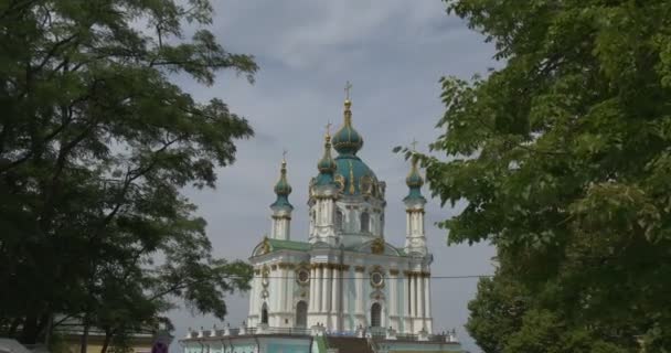 A Igreja de Santo André, o principal edifício de estilo barroco em Kiev, visto através dos ramos de árvores verdes caducas em um clima nublado — Vídeo de Stock