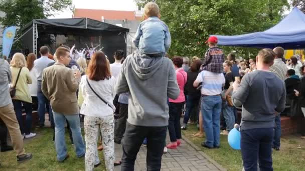 Mucha gente mira una actuación con artistas jóvenes, que bailan, gritan y entretienen al público en una pequeña escena de tienda en una zona de parques en Polonia — Vídeo de stock
