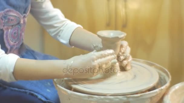 Een ambachtelijke aardewerk is gemaakt door een klein meisje, gekleed in blauwe schort en witte Blouse, die probeert om haar eigen klei Pot produceren — Stockvideo