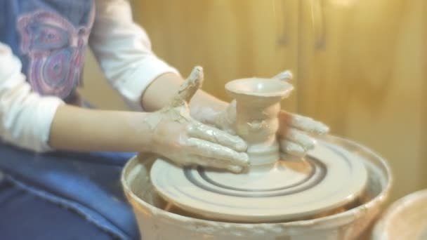 Eine Tasse aus Ton wird von einem kleinen blonden Mädchen in weißer Bluse und blauer Schürze gemacht, während sie das Töpfern lernt — Stockvideo