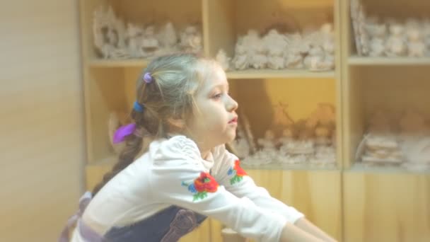 Dans un atelier de poterie une jeune fille de six ans se lave les mains après avoir fait ses propres pots d'argile et tasses, étant habillée d'une blouse blanche et tablier bleu — Video