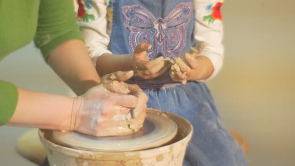 Een ambachtelijke aardewerk is gemaakt door een klein meisje, gekleed in blauwe schort en witte Blouse, die probeert om haar eigen klei Pot produceren — Stockvideo