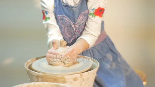 Qualche tazza di argilla è fatta da una piccola ragazza bionda vestita con una camicetta bianca e un grembiule blu e una signora esperta, aiutandola con questa procedura — Video Stock