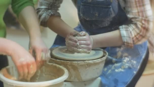Un apprenti en chemise ébouriffée avec un tablier et un maître en chemisier vert font de l'artisanat de poterie ensemble dans un atelier spécial avec une roue en pot — Video