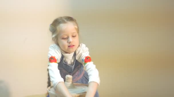 Prächtiges sechsjähriges blondes Mädchen arbeitet tagsüber an einer Töpferscheibe, trägt weiße Bluse und Jeansschürze — Stockvideo