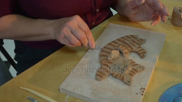 Una dama profesional está haciendo un gato de arcilla divertido en una tabla de madera, utilizando alguna herramienta específica, y una niña está haciendo su propio regalo — Vídeos de Stock