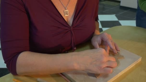 Een Blonde vrouw is het maken van een indrukwekkend Clay speelgoed op een houten plank en een klein meisje is helpen haar terwijl zitten aan dezelfde tafel — Stockvideo