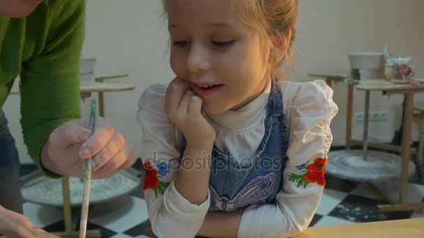 Um brinquedo de barro é feito por uma mulher de meia-idade trabalhosa e uma menina aprendiz de seis anos, olhando para as mãos de um mestre na Polônia — Vídeo de Stock