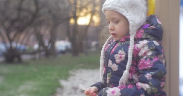 Pequeña chica rubia está jugando en una zona de parque vestida con un chaleco de color, sombrero de punto con balabón, pantalones rosados, en otoño en Polonia — Vídeos de Stock