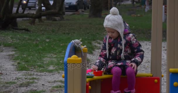 Une petite fille de six ans joue dans la cuisine, tout en étant dans un bac à sable coloré non loin de sa maison en automne — Video