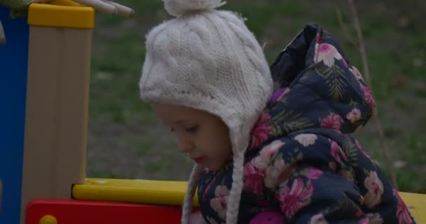 Fille blonde de six ans joue dans une zone de parc habillé d'un gilet coloré, bonnet tricoté avec balabon, pantalon rose, en automne en Pologne — Video