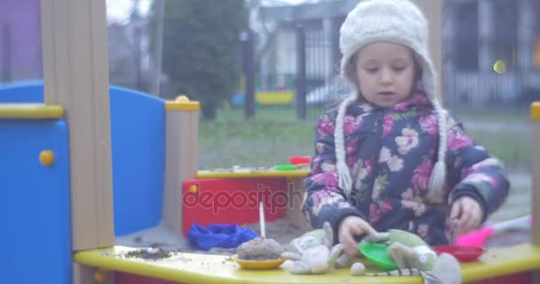 Färgade trä lekplats med Sand och en liten flicka i en vit Stickad mössa och färgade Waiscoat snygga där inte långt från ett hus i höst — Stockvideo