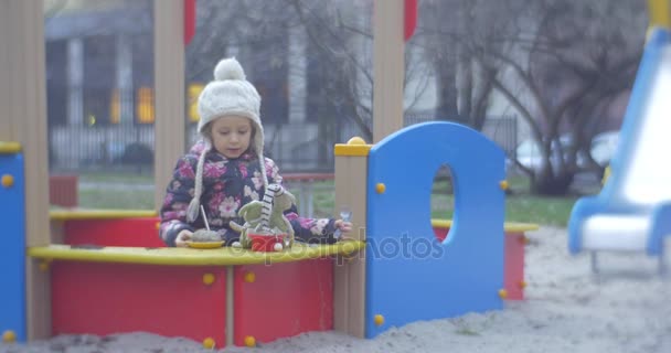 Šesti let stará blondýna dívka je hrací v parku zóny oblečené v barevných Waiscoat, pletené čepice s Balabon, růžové kalhoty, na podzim v Polsku — Stock video