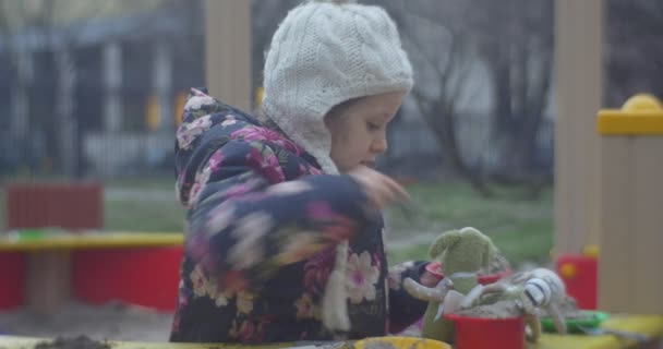 Een aantrekkelijke Blonde meisje is leggen uit haar speelgoed op een enkele halve ronde gekleurde Bench voor kinderen, terwijl op een speelplaats, — Stockvideo