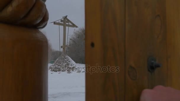 Рука человека закрывает древние деревянные ворота церкви Православный Крест, установленный перед Христианской деревянной наброской Всех Святых в Святогорской лавре Зимой — стоковое видео