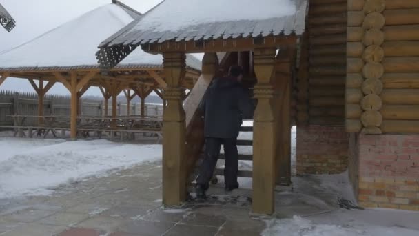 Человек исследует деревянный терем, поднимающийся по лестнице в Христианском монастыре Скит Всех Святых Святогорской лавры в зимний экскурсионный туризм — стоковое видео