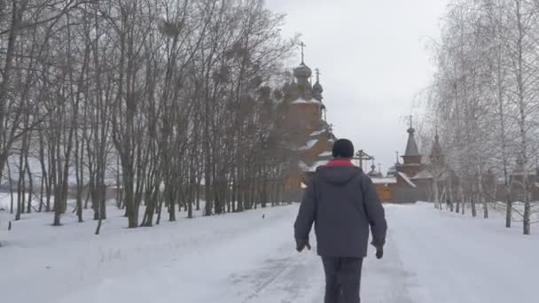 O turista adorador vai ver a Igreja Antiga caminhando pelo beco para o mosteiro de madeira chamado Skit Vsekh Svyatykh Winter View of Historical Sights — Vídeo de Stock