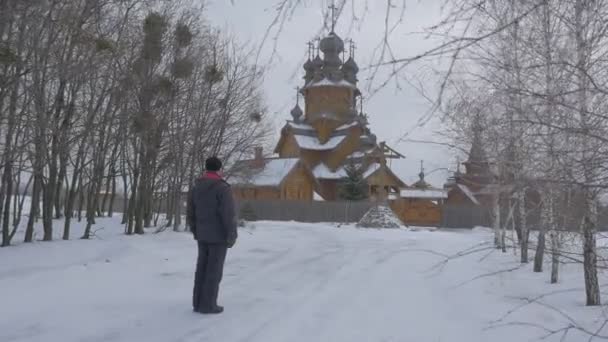 男人走过雪巷十七世纪教会木制的基督教修道院小品 Vsekh Svyatykh Sviatogorskaya 修道院宗教人胸前划着十字 — 图库视频影像