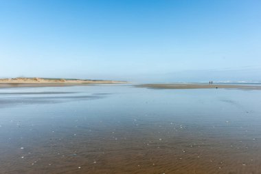 Çift boyunca geniş düz kumsalda yürüyen küçük uzak rakamlar 