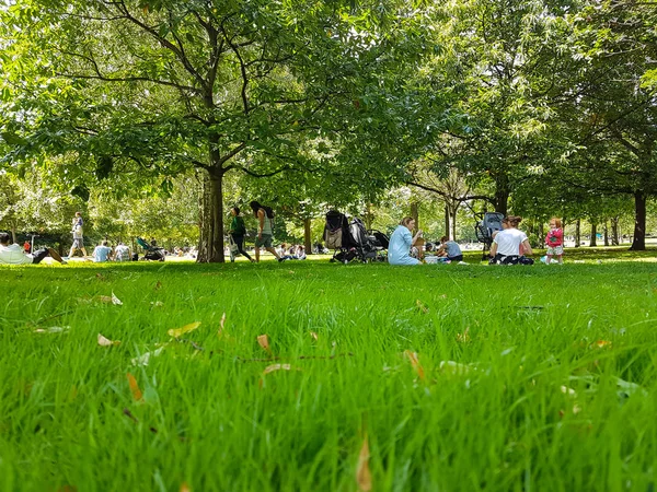 People including family groups seated on grass and walk amongst the trees in Victoria Park — Stock Photo, Image
