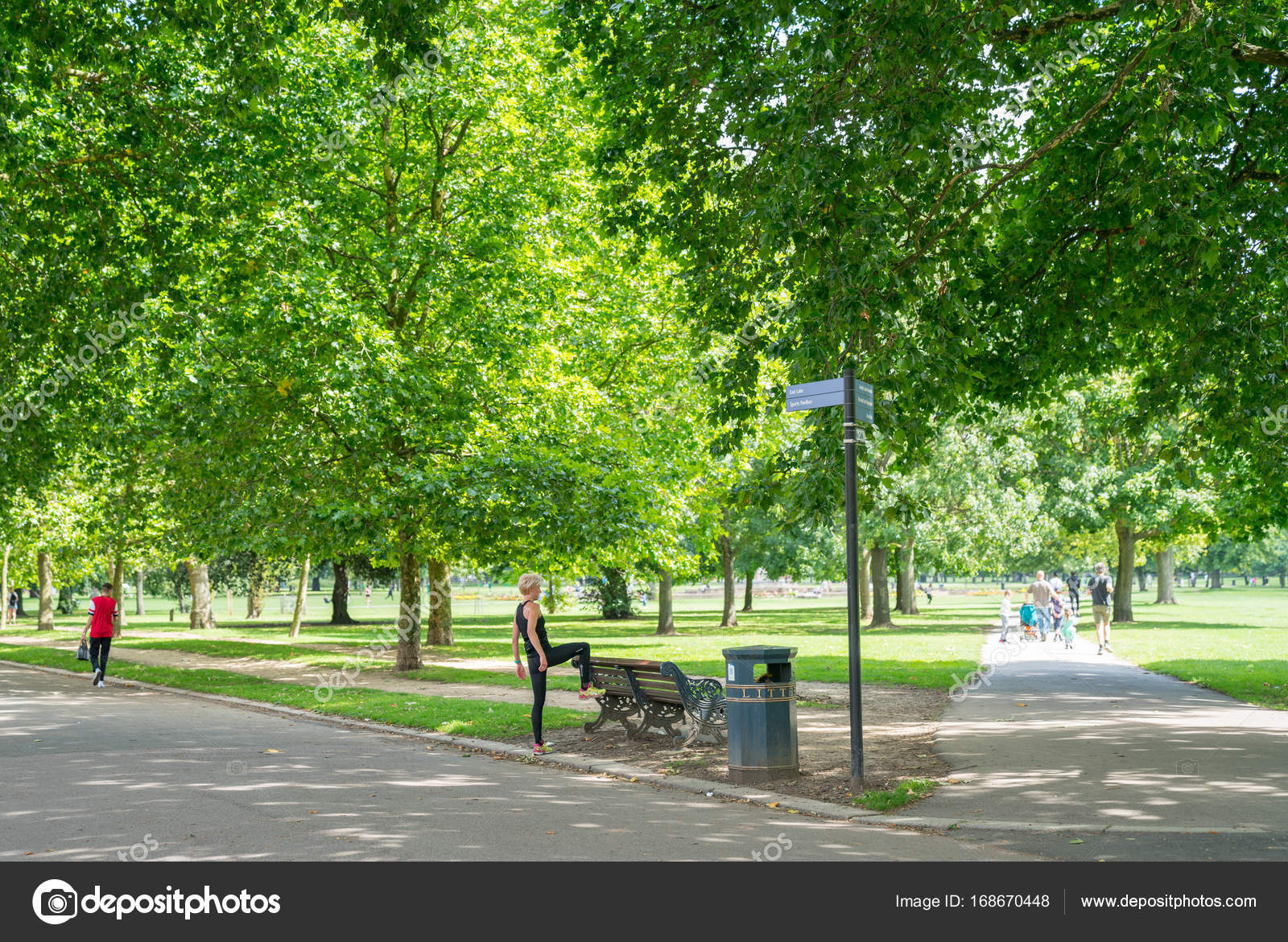 Blond Haired Woman In Exercise Clothing Stretches On Park Bench
