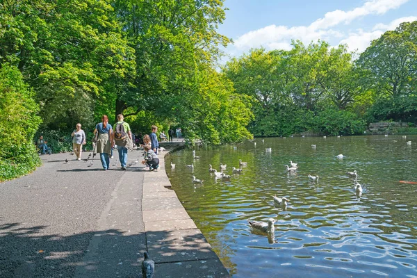 La gente disfruta paseando por el estanque mientras los niños alimentan patos —  Fotos de Stock