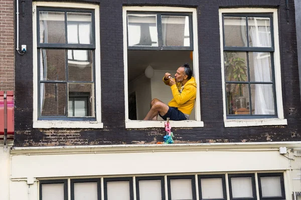 Homem em yeloow capuz sititing na janela no apartamento do primeiro andar — Fotografia de Stock