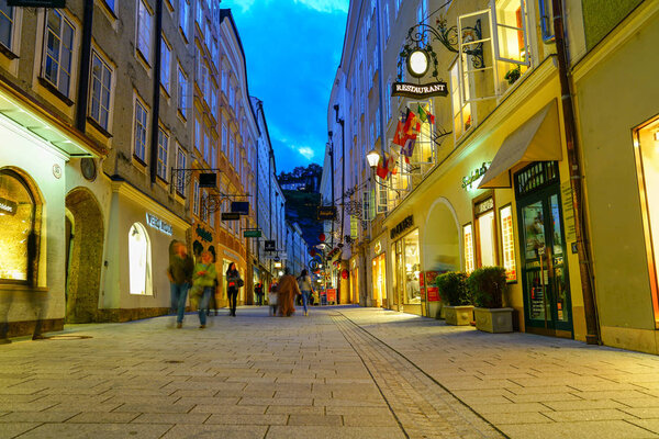 SALZBURG, AUSTRIA - SEPTEMBER 6 2017; Street scene, people blurred walking along narrow road between modern shops in traditional buildings in old town under night lights from shops.