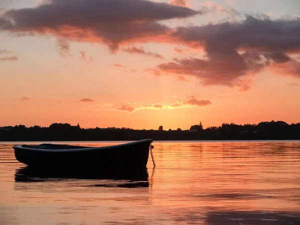 Kleines Schlauchboot schwimmend auf rotem Hafenwasser bei Sonnenuntergang — Stockfoto