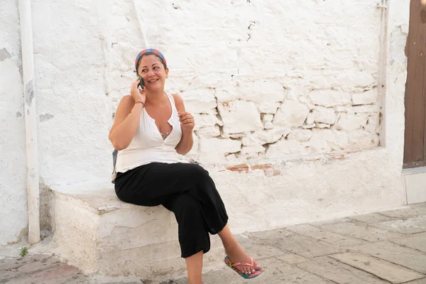 Woman sitting in front rustic whitewashed wall on mobile phone — Stock Photo, Image