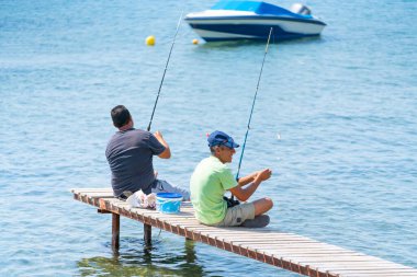 Küçük bir iskelede balık tutan iki adam.