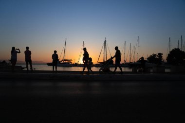 Güneşin doğuşunu ve yatın direğini hayranlıkla izleyen insanların siluetleri.