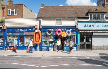İnsanlar ellerinde plaj oyuncaklarıyla Georges Mini Market 'in önünden geçiyorlar. 