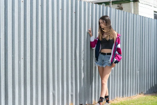 Moderna adolescente em pé por cerca de ferro ondulado fundo — Fotografia de Stock