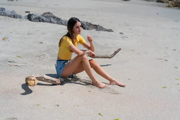 Teenage girl in yellow top and denim shorts sitting on piece of — Stock Photo, Image